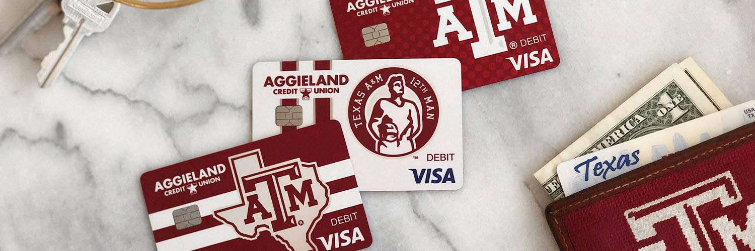 three styles of Texas A&M-branded Aggieland Credit Union debit cards spread out on a marble countertop surrounded by a wallet and keys