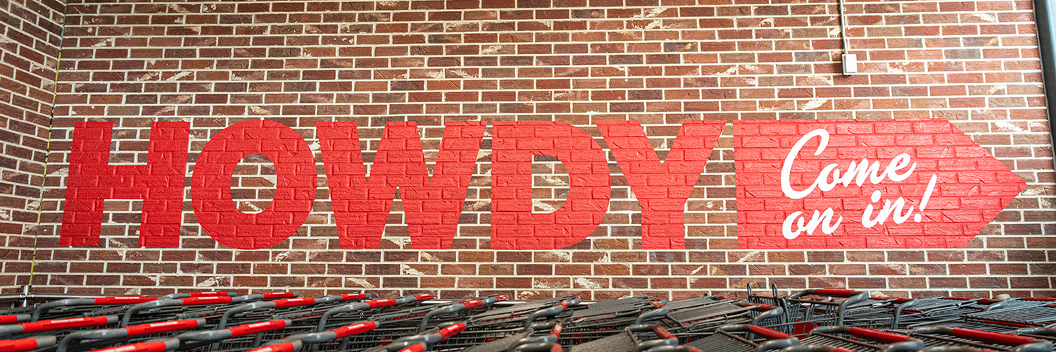  'Howdy! Come on in!' painted in red on a brick wall above rows of shopping carts