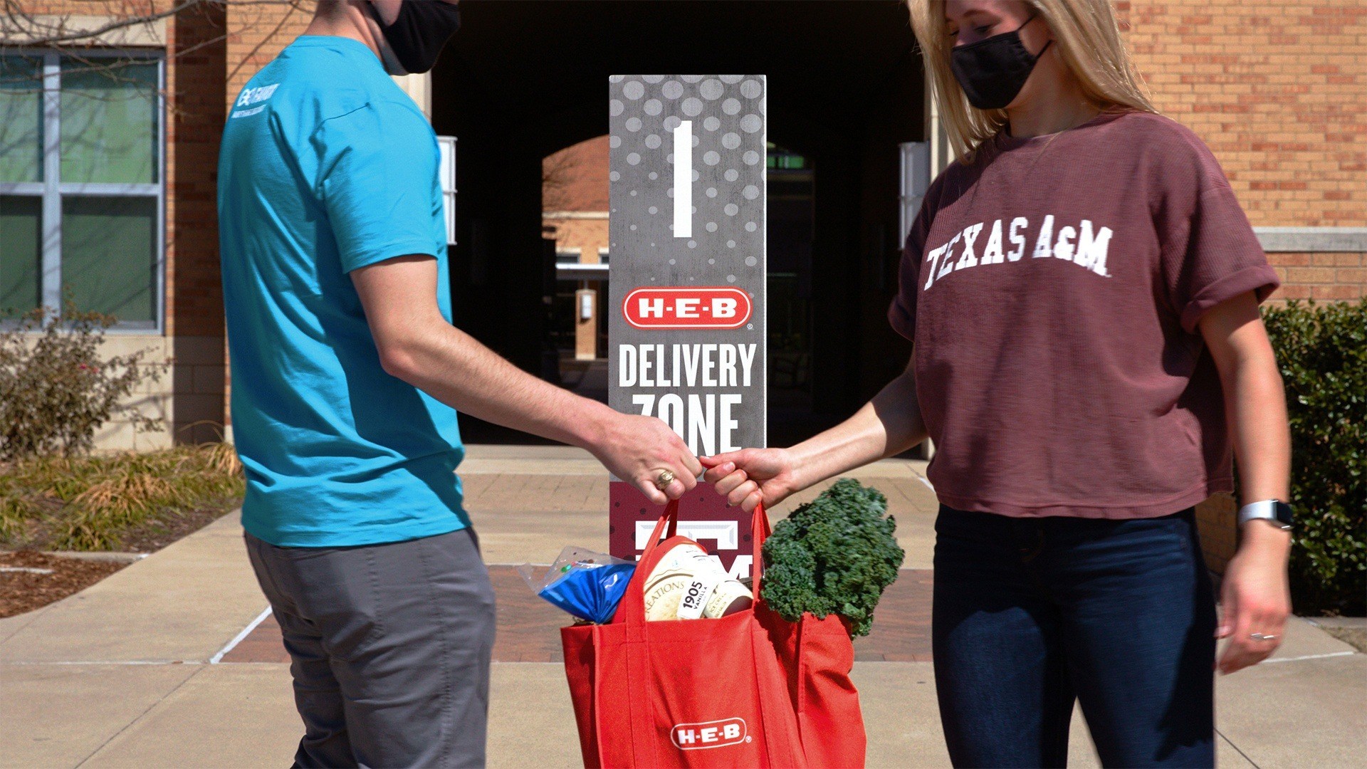 an HEB employee hands a Texas A&M student their order at a designated delivery zone on campus