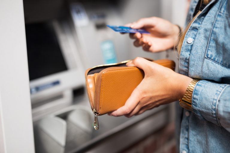 person holding their wallet and debit card at an ATM machine