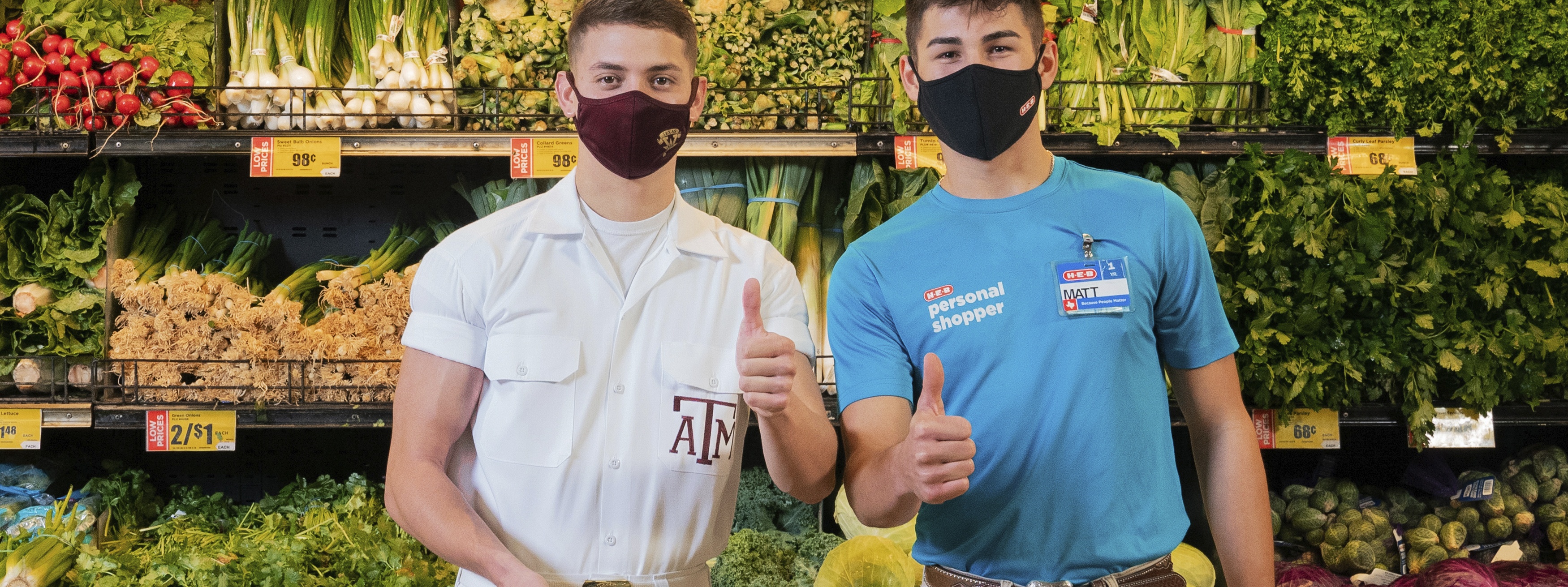 H-E-B employee and Texas A&M yell leader stand next to each in front of the produce section at H-E-B